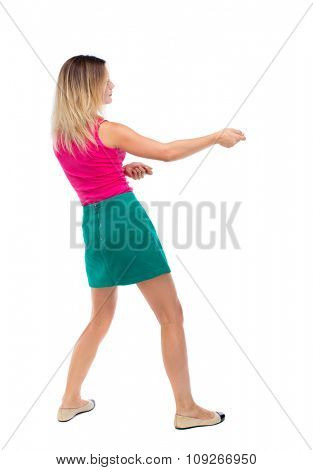 back view of standing girl pulling a rope from the top or cling to something. girl  watching. Rear view people collection.  . The blonde in a green skirt and pink sweater leaning legs pulls the rope.