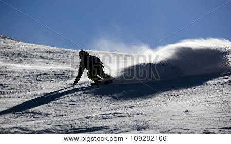 Backlit skier splashing snow powder while turning and skiing fast