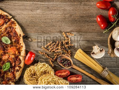 Italian food background with pizza, raw pasta and vegetables on wooden table
