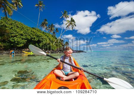 Little girl enjoying paddling in colorful orange kayak at tropical ocean water during summer vacation
