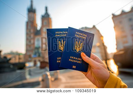 Female hands holding Ukrainian abroad passports on the Krakow city center background