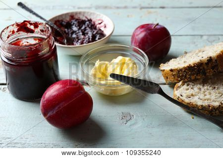 Tasty jam in the jar and bowl, butter, fresh bread and plums on blue wooden background