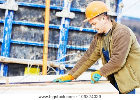 Concrete work. Male builder carpenter worker cutting plywood for falsework construction before concreting at building site