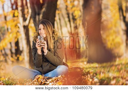 Young woman drinking coffee in autumn in park