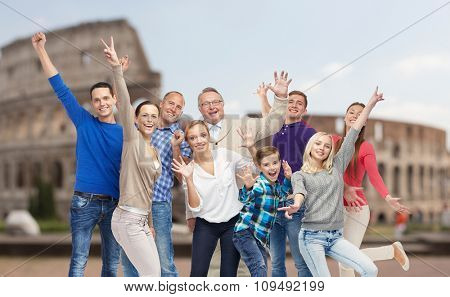 family, travel, tourism and people concept - group of happy men, women and boy having fun and waving hands over coliseum background