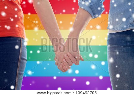 people, homosexuality, same-sex marriage, gay and love concept - close up of happy lesbian couple holding hands over rainbow flag background over snow effect
