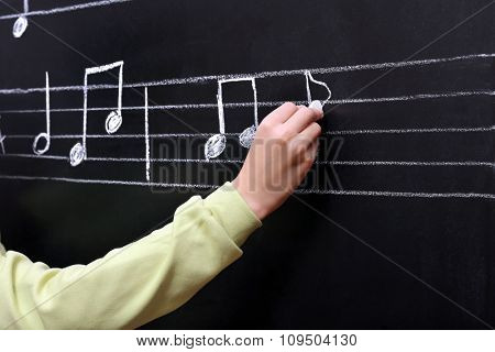 View on boy's hand writing at the blackboard with musical notes, close-up