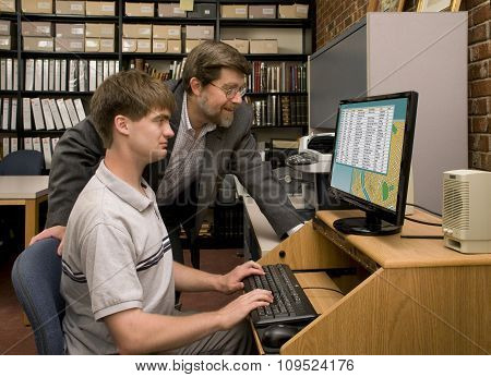 Man Guiding A Student In A Database Search In An Archive