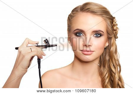 portrait of a beautiful young blonde woman on a light background. there is hand with aerograph makin