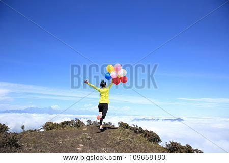 young woman with balloons on mountain peak