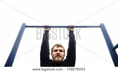 young man doing pull ups on horizontal bar outdoors
