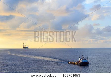 Offshore Jack Up Drilling Rig And Supply Boat In The Middle Of The Ocean During Sunset Time
