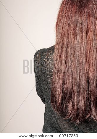 Rear view of a young woman with long brown hair against gray background copyspace