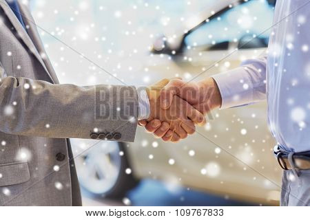 auto business, car sale, deal, gesture and people concept - close up of male handshake in auto show or salon over snow effect