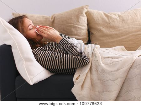 Portrait of a sick woman blowing her nose while sitting on the sofa