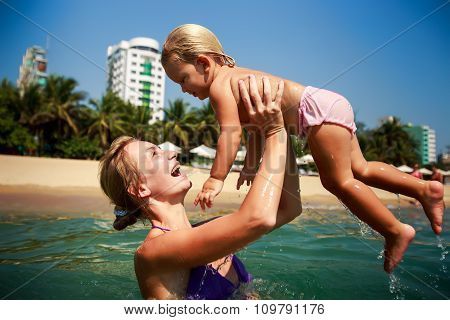 Side-view Mother In Sea Laughs Holds In Arms Small Daughter
