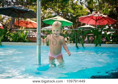 Small Blonde Girl Smiles Holds Pole In Shallow Water Of Pool