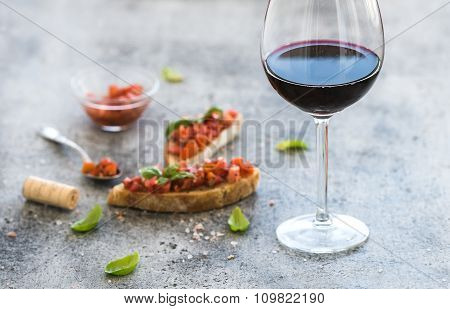 Wine appetizer set. Glass of red wine, brushettas with fresh tomato and basil on over rustic grunge