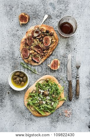 Rustic homemade pizzas with eggpant, cheese, olives, arugula, prosciutto and figs over grunge backdr