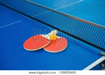 pingpong rackets and ball and net on a blue pingpong table