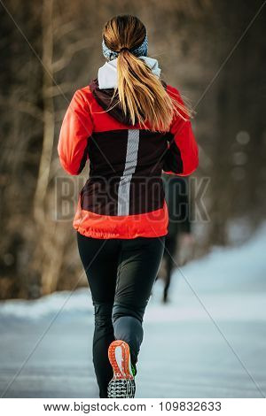 closeup young woman runner running on snow-covered alley in a winter Park