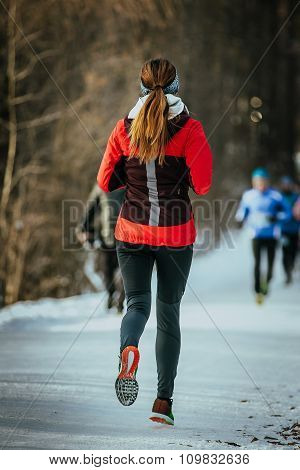 young woman runner running on snow-covered alley in a winter Park. rear view