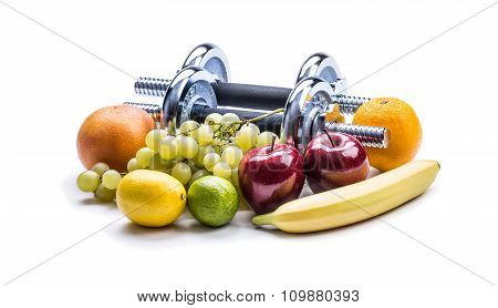 Chrome dumbbells surrounded with healthy fruits measuring tape on a  white background with shadows.