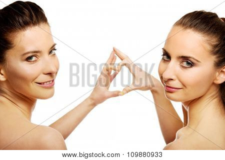 Two beautiful women making heart with fingers.