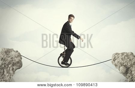 Brave business man riding an mono cycle between cliffs concept
