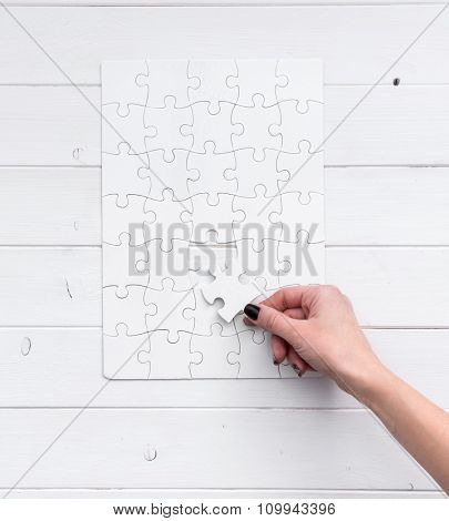 hand holding a piece of white uncompleted puzzle on white wooden background