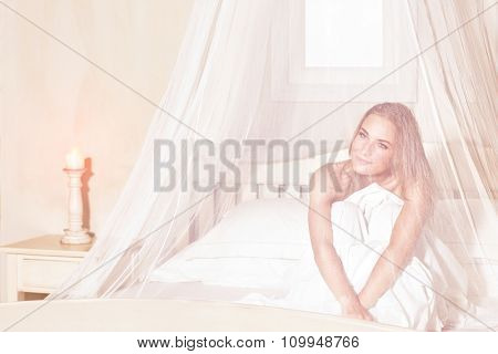 Romantic woman sitting in the bed under gentle transparent valance, spending weekend in luxury spa hotel, enjoying rest and relaxation