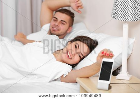 Happy couple waking up with mobile alarm clock