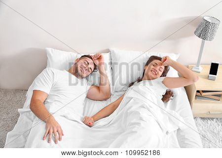 Happy couple waking up with mobile alarm clock