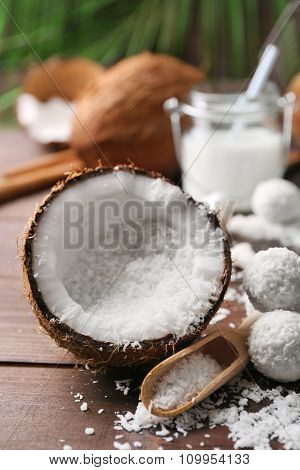 Candies in coconut flakes, glass of milk and fresh coconut on dark wooden background