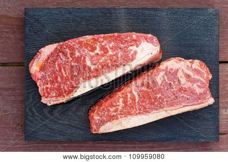 Two pieces of raw striploin steak on wooden plank