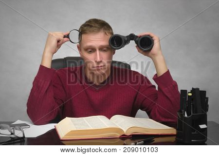 Yound student man with binoculars and magnifier in hands tired of studying and searching information. Business man tired of boring work. Hard job. Find and search.