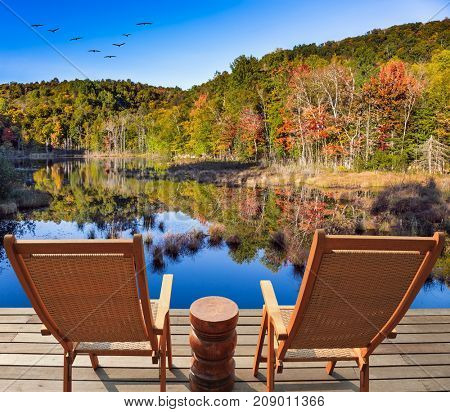 Flock of migratory birds flies over the lake. Wooden comfortable loungers on the shore of the lake. Resort in French Canada - Mont Tremblant. Concept of ecological tourism