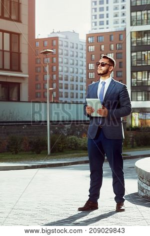Real estate agent with tablet computer stands on modern city backdrop. Businessman or business concept