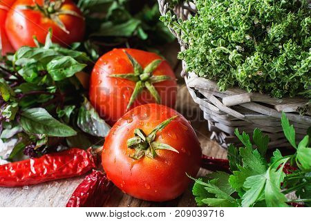 Ripe Fresh Organic Tomatoes Provence Herbs Thyme Basil in Wicker Basket Hot Chili Peppers on Wood Table. Rustic Kitchen Interior. Soft Day Light