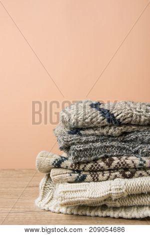 Stack of Handmade Warm Knitted Socks Scarfs Mittens Sweaters From Rough Wool Yarn Brown Beige Grey. Wood Table Peach Color Wall Background. Eco Fashion Kinfolk Style. Natural Materials