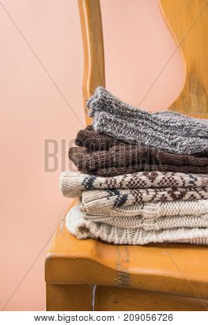 Stack of Handmade Warm Knitted Socks Scarfs Mittens Sweaters From Rough Wool Yarn Brown Beige Grey on Vintage Chair Trendy Peach Color Wall Background. Eco Fashion Kinfolk Style. Interior