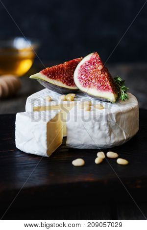 Brie, camambert cheese, fresh purple figs, nuts and honey on dark wooden backdrop. Closeup view, vertical