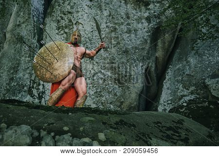Brave medieval warrior ready to attack with a sword standing on top of a rock covering himself with a shield copyspace.