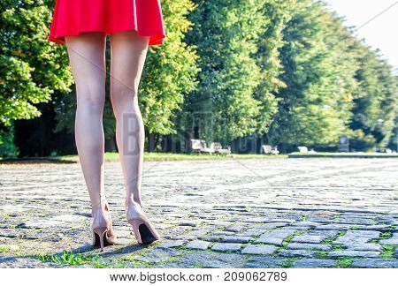 legs of a woman standing on a paving stone in a parko on sunny summer day