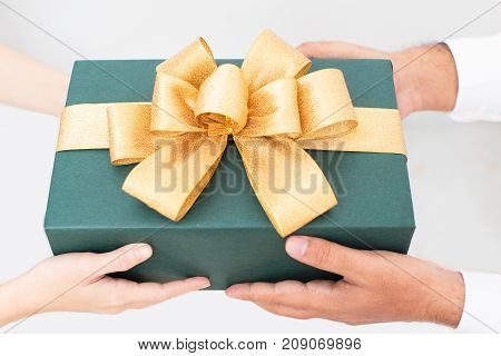 Beautiful packaged Christmas gift with yellow ribbon in hands of couple. Friends celebrating New Year and giving gift. Gift box with bow. Presenting gift concept