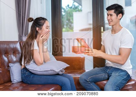 Couple lover romantic sweet interior indoor concept Young asian together man holding surprise box heart gift to woman on sofa in home at living room relax and resting happy