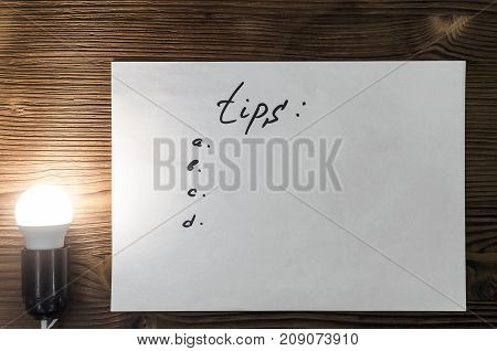 Tips note paper page on wooden desk table surface background with copy space in the light of burning bulb lamp.