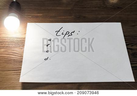 Tips note paper page on wooden desk table surface background with copy space in the light of burning bulb lamp.