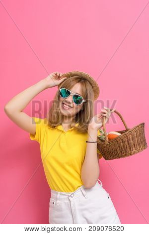 Fashion portrait of girl shopping concet. young beautiful asian with relax dress yellow shirt and white jeans pants hat sunglasses basket vegetables in summer lifestyle on pink background.