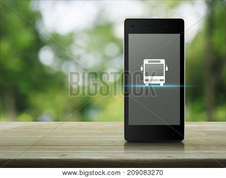 Bus flat icon on modern smart phone screen on wooden table over blur green tree in park Business transportation service concept